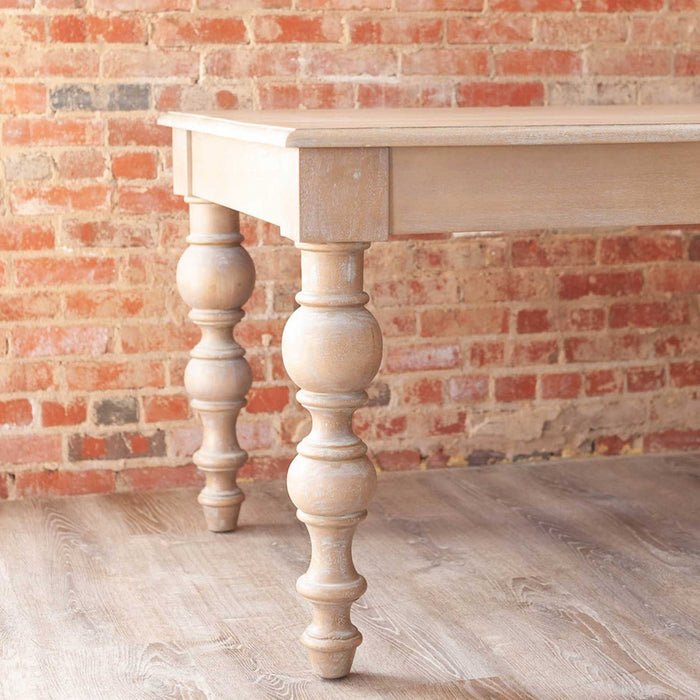 Angled view of end of sand-colored dining table with rounded legs.