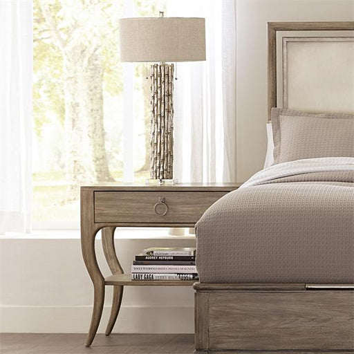Sand colored nightstand beside bed with lamp.