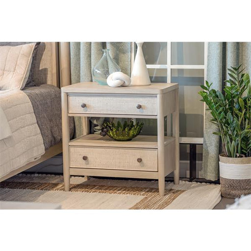Sand colored nightstand beside bed with lamp and decor.