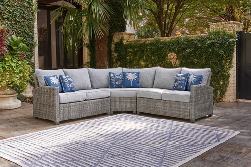 Backyard patio area with palm trees and gray wicker sectional, blue pillows.
