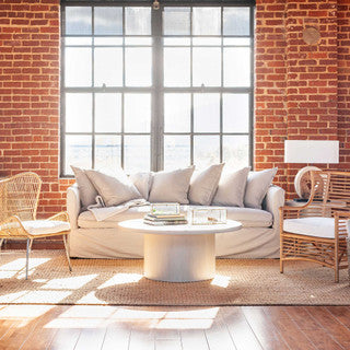 Airy brick living room with pillow-filled white couch and wicker chairs.