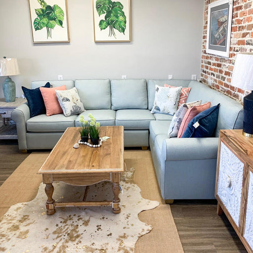 White and brick wall living room with light blue sectional and wood table.